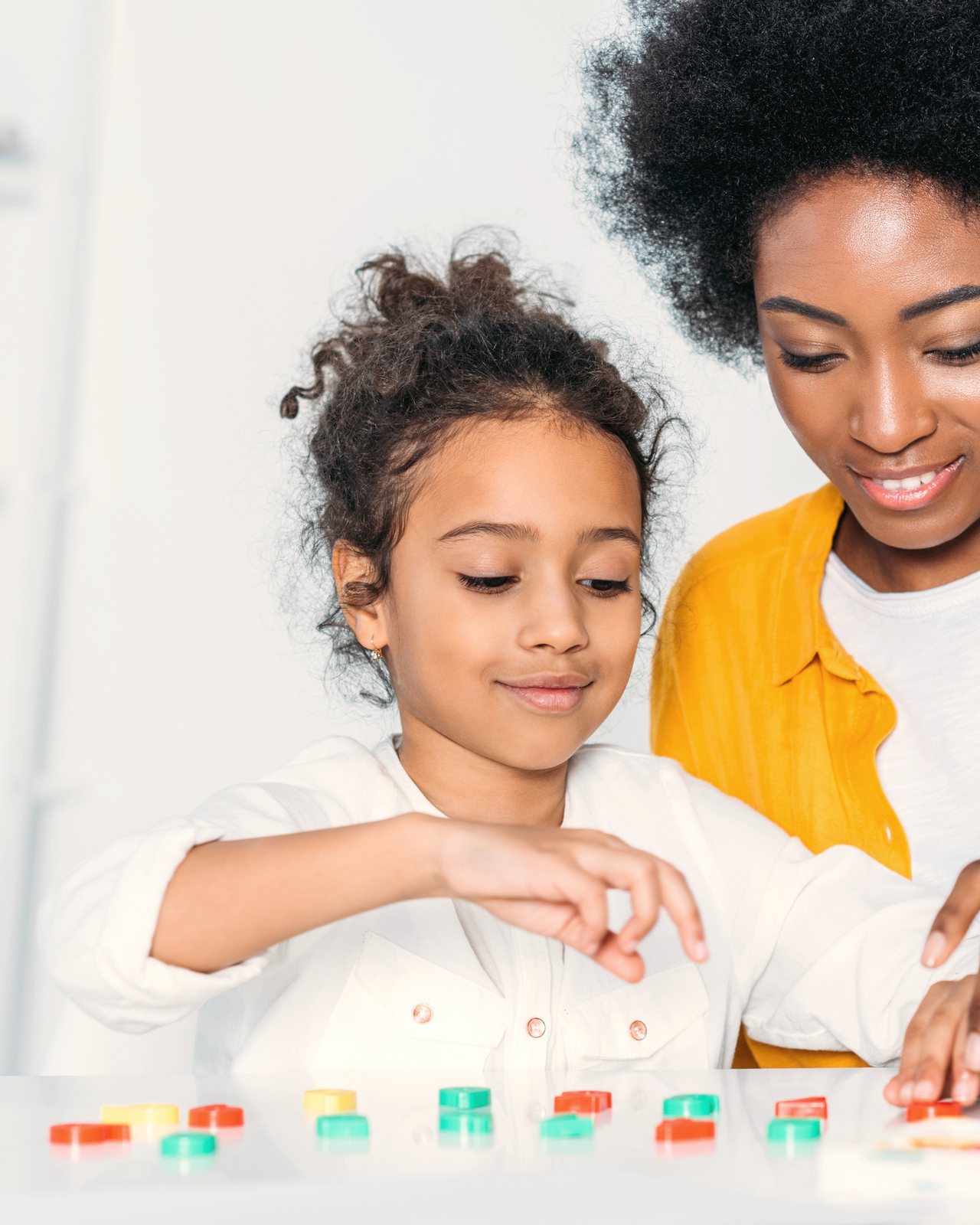 A smiling woman and young girl sort colorful counting toys at a table