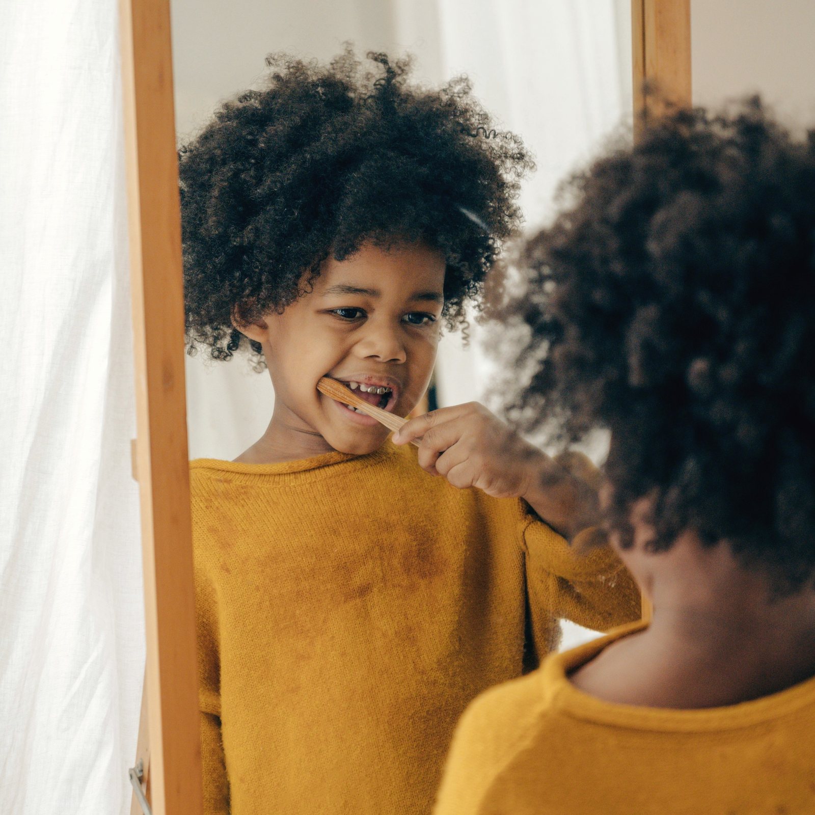A boy brushes his teeth in front of a mirror