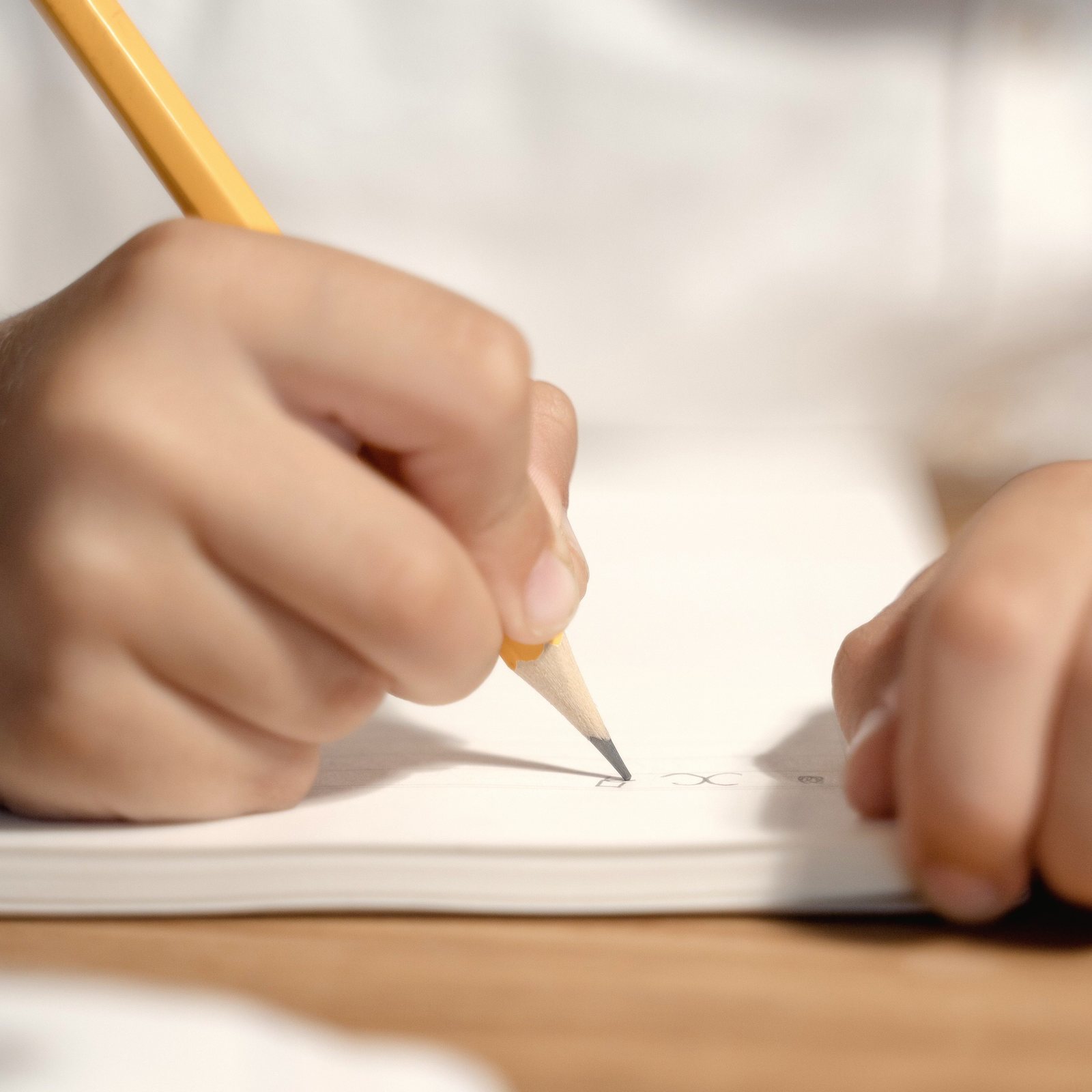 A hand writes with a yellow pencil in a notebook