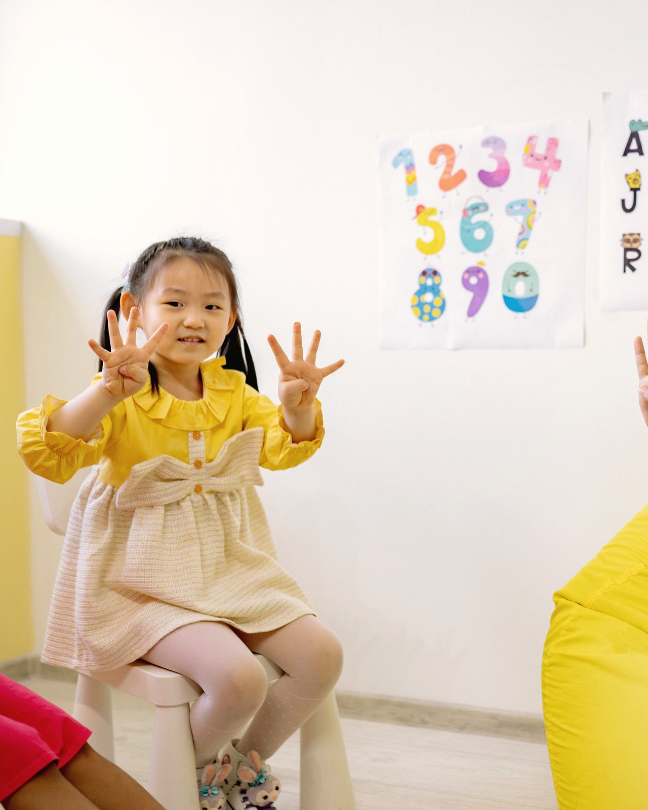 A young girl in a yellow dress counts on her fingers in a classroom