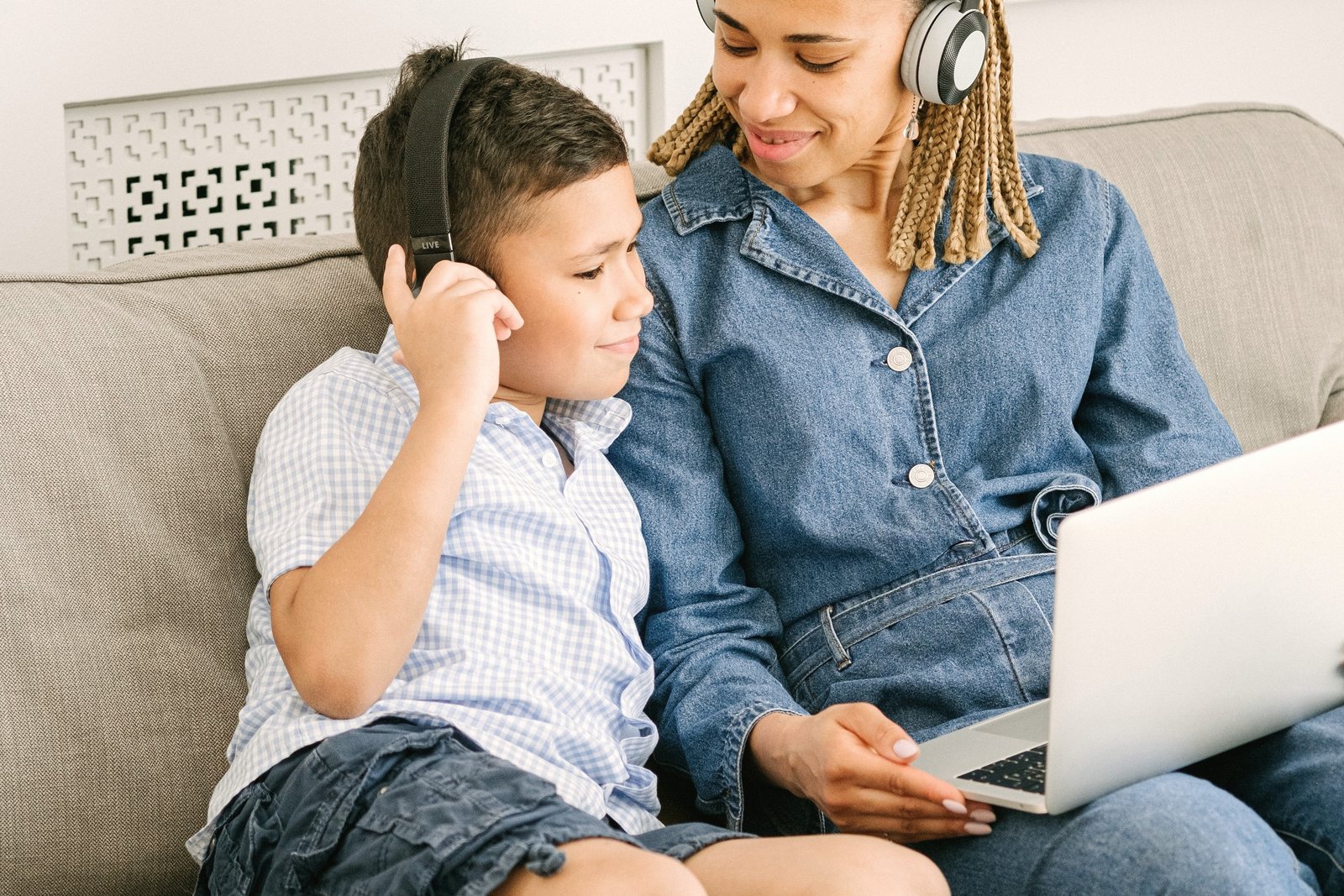 A mother works on a laptop on the sofa while her son sits beside her