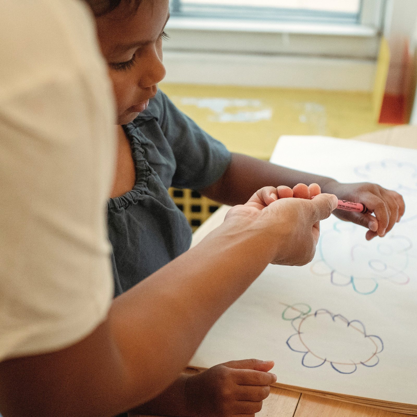 An adult helps a young girl draw flower shapes at a table