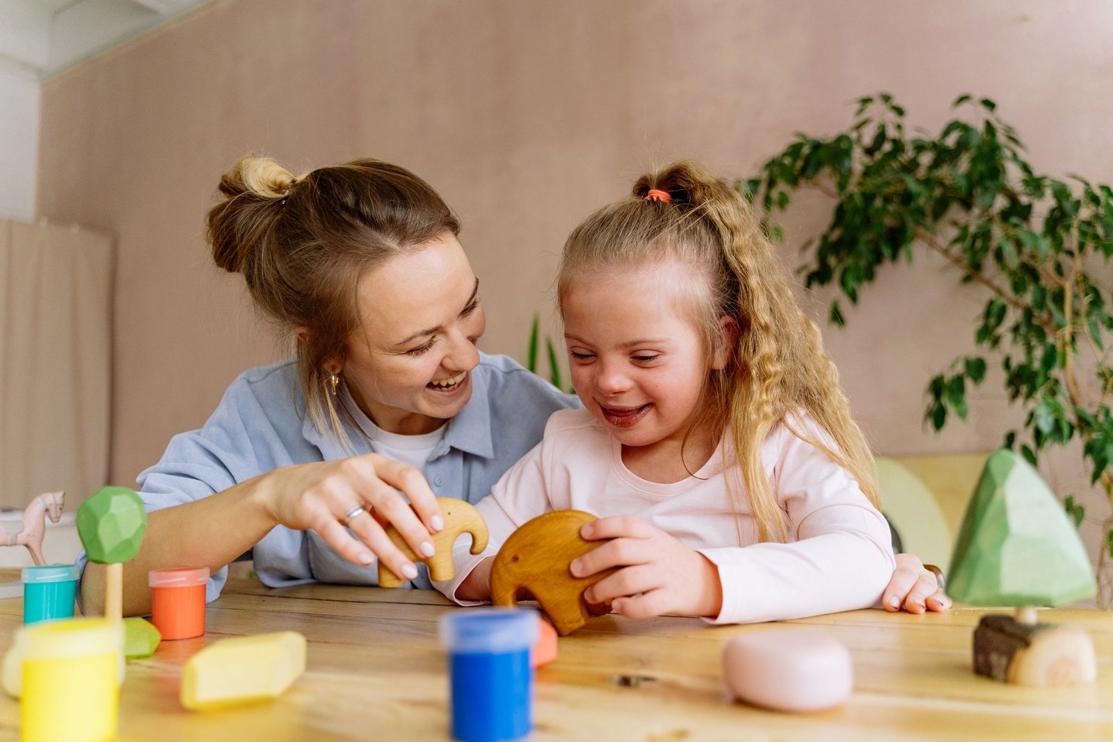 A smiling therapist and a young girl play with wooden toys at a table