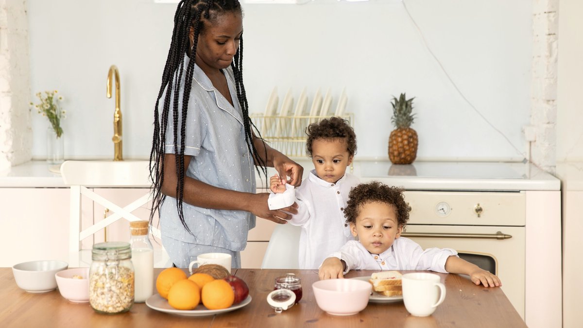 Mom helping her toddler wipe his hands at the breakfast table, an everyday self-care routine